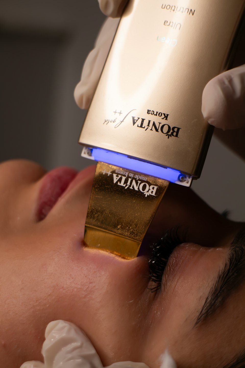 Professional applying golden ultrasonic device to client's cheek.