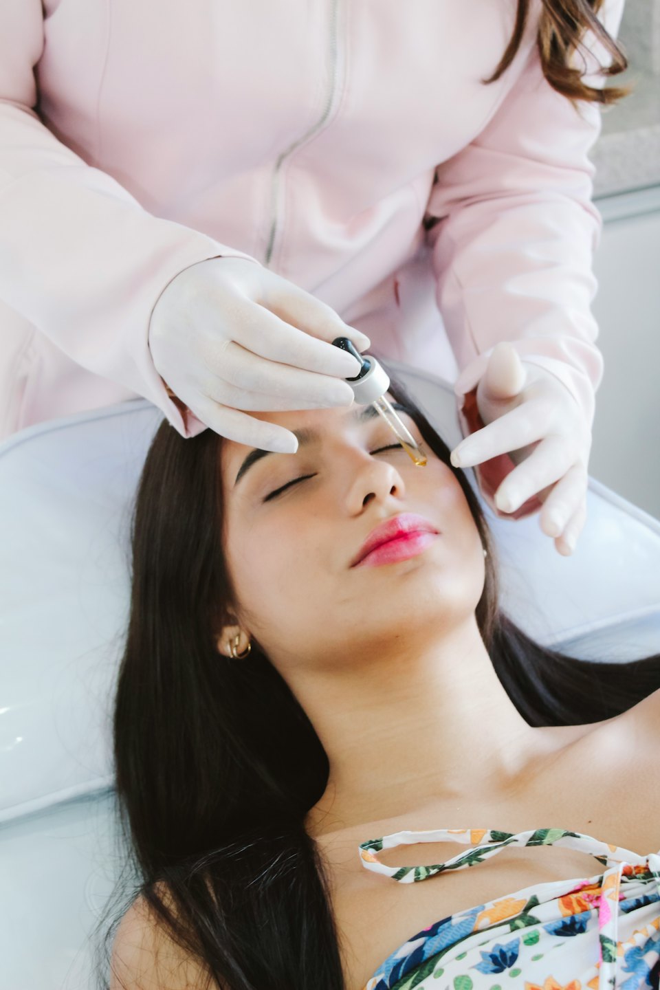 Skincare professional applying yellow serum to woman's cheek.